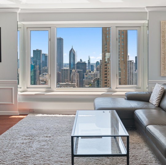 Living room with a gray sectional and glass coffee table overlooking the city skyline.